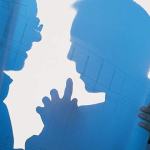 A silhouette of two men looking at a large piece of rolled out paper with blueprints on it.