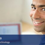 A man at a desk with his laptop looking back over his shoulder at the camera, with a blue banner on the botom of the image that reads "Six Sigma - information technology" in large white letters.