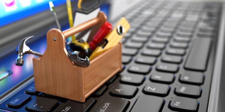 Close up of a very small toolbox on the the keyboard of a laptop filled with hammers, saws, levels, and other small tools.