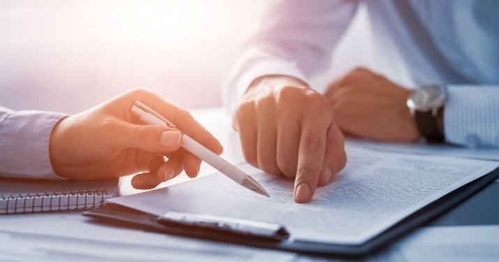 Close up photo of the hands of two people going over a contract on a clipboard and pointing out a specific detail.