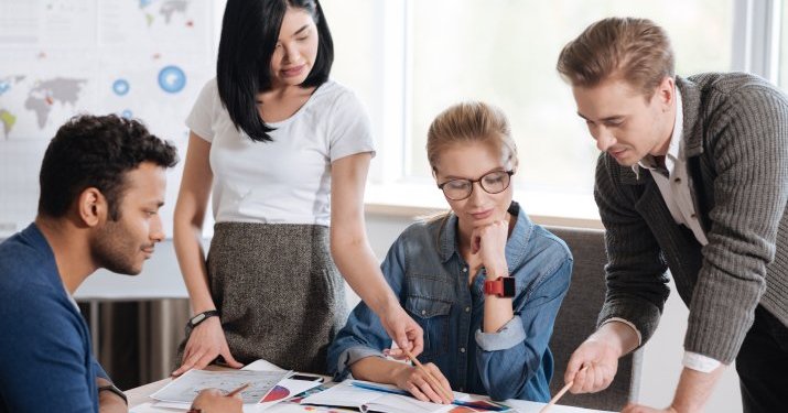 A group of HR employees standing around a table focusing on one book, working together on company initiatives.