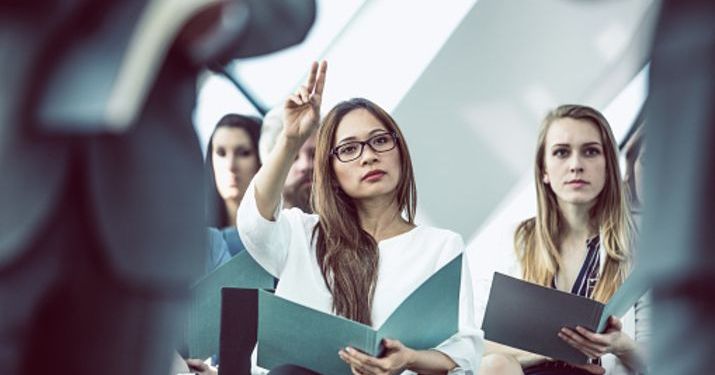 A small group of female HR students holding notebooks and listening to a lesson while one student is raising her hand.