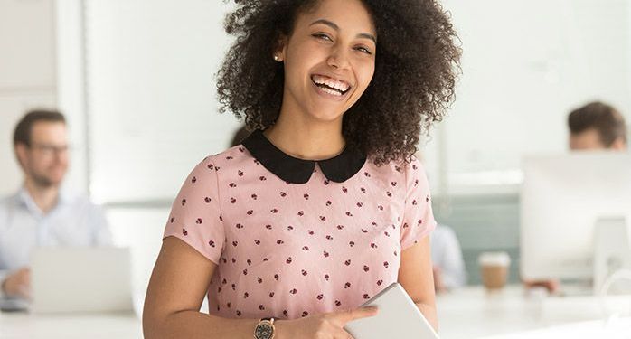 A woman wearing a pink shirt in an office holding a smart tablet.