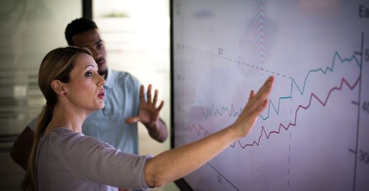 A businesswoman giving a presentation on data analysis and potential cost benefits.