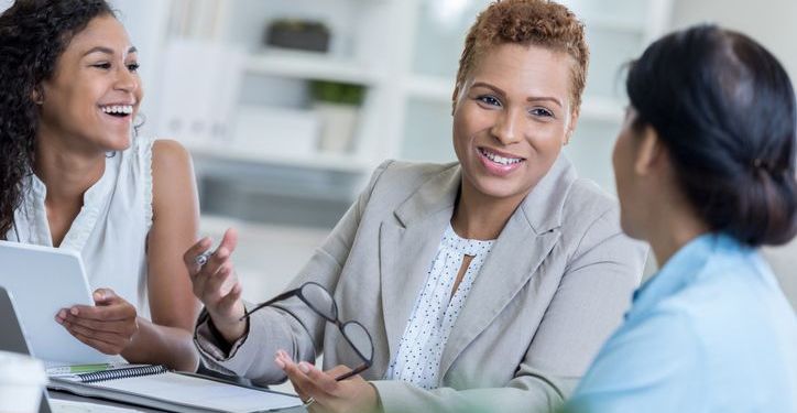 Organizational Leadership depicted as businesswoman discusses a project with her team.