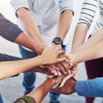 Closeup shot of a group of people joining hands in a huddle