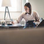 Woman sitting an home on laptop writing notes