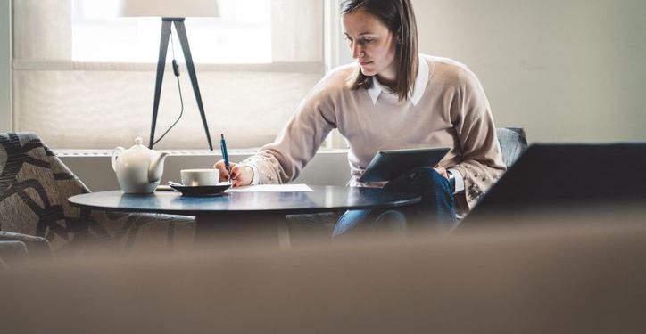 Woman sitting an home on laptop writing notes