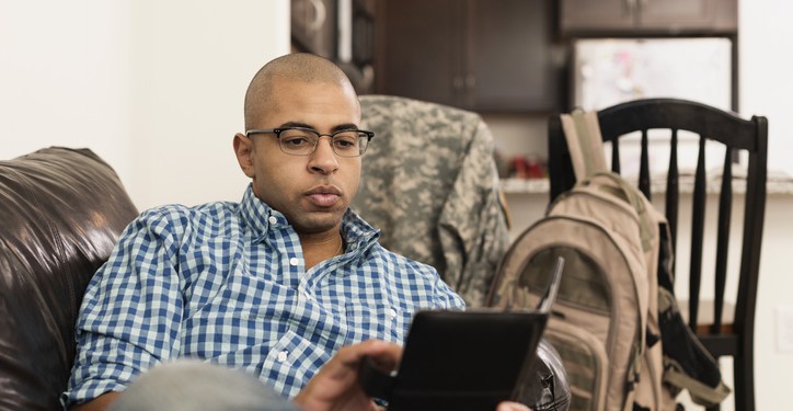 Mixed race servicemember using digital tablet on sofa in living room.