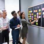 Diverse group of project team members standing in front of a sticky board looking at list of projects