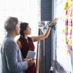 Man and woman looking at colorful adhensive notes on whiteboard in an office