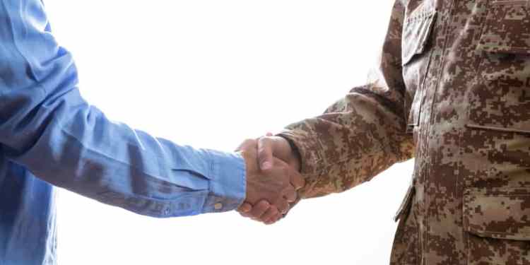 Military person and civilian shaking hands standing on white background