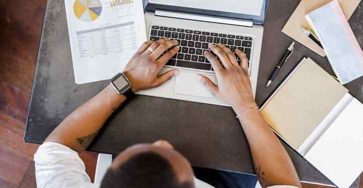 Man working on data reports using laptop at desk in home office