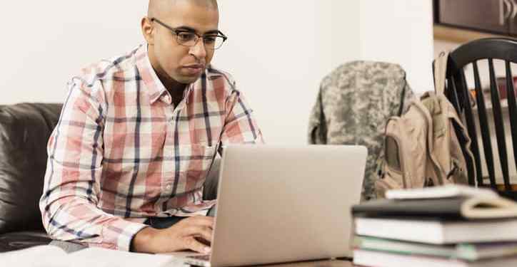 Mixed race soldier using laptop at home